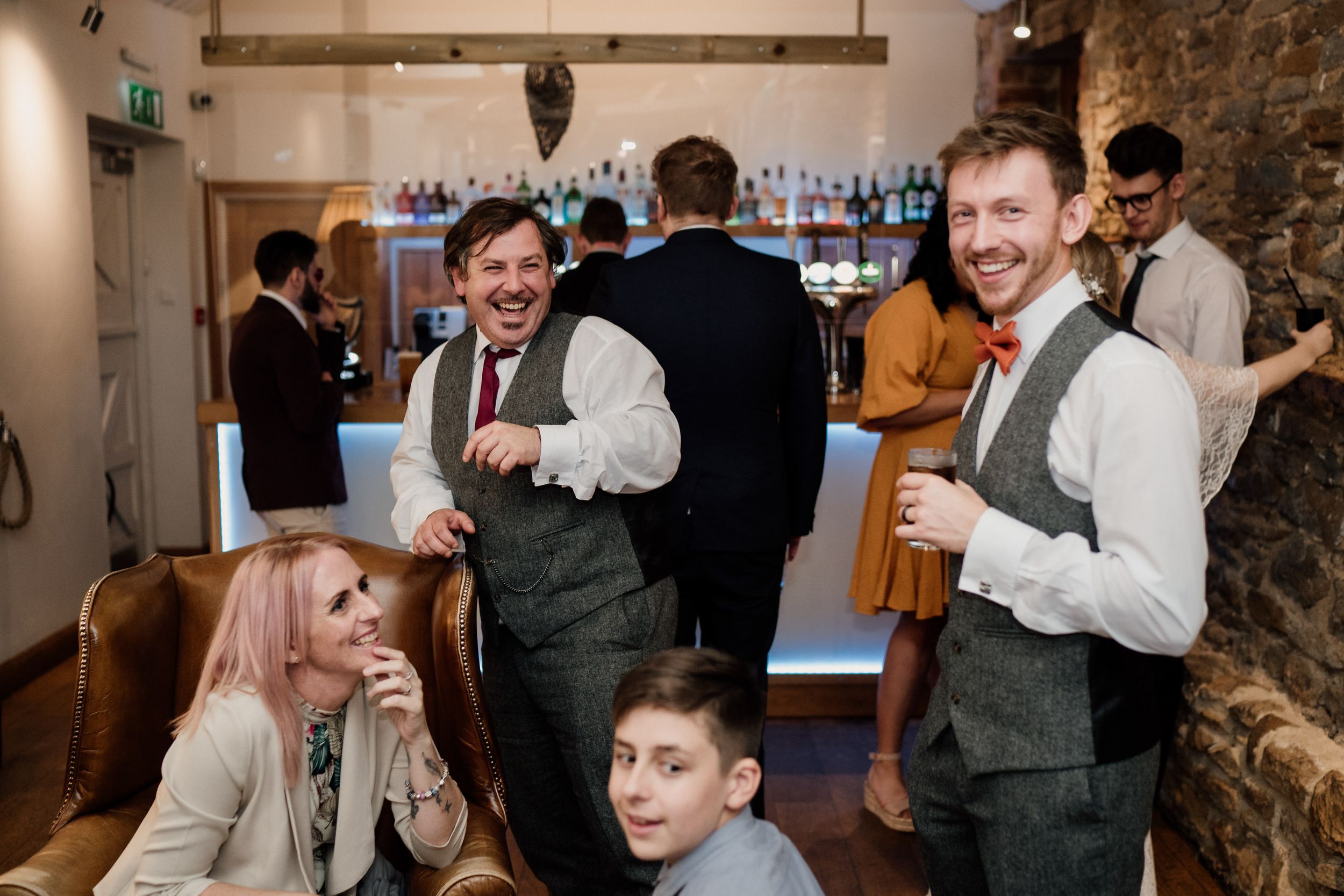 Guests share laughs at wedding reception in rustic venue with exposed brick walls.
