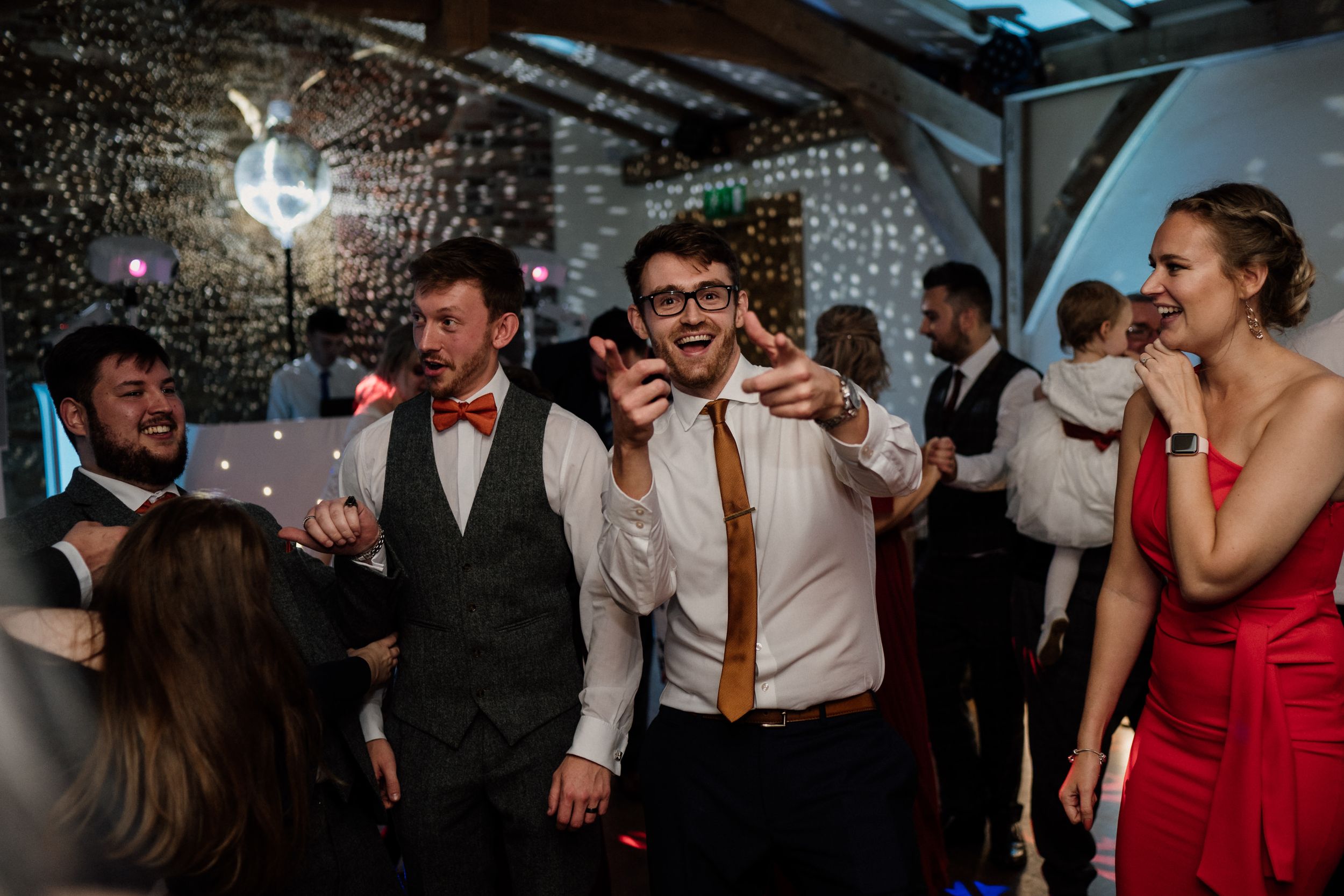 Party goers celebrate energetically on a dance floor under twinkle lights.