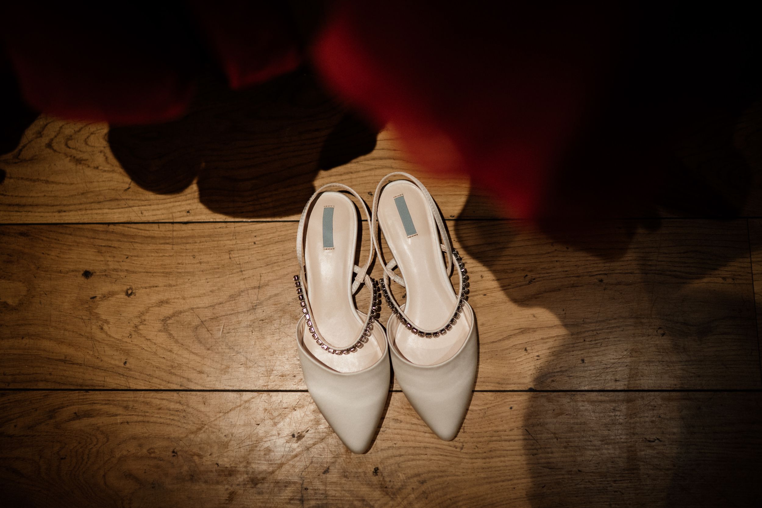 Elegant white bridal shoes with pointed toes on wooden flooring.