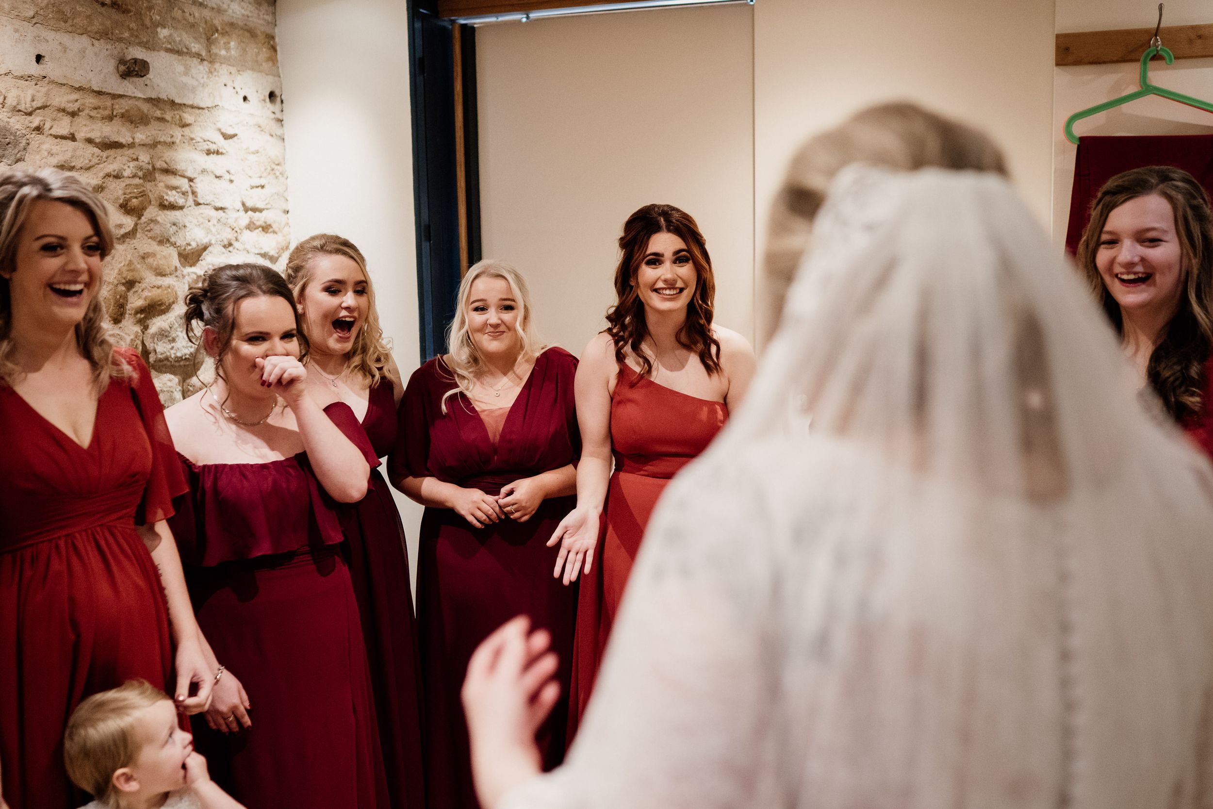 Wedding party in deep red dresses reacting with joy during a special moment.