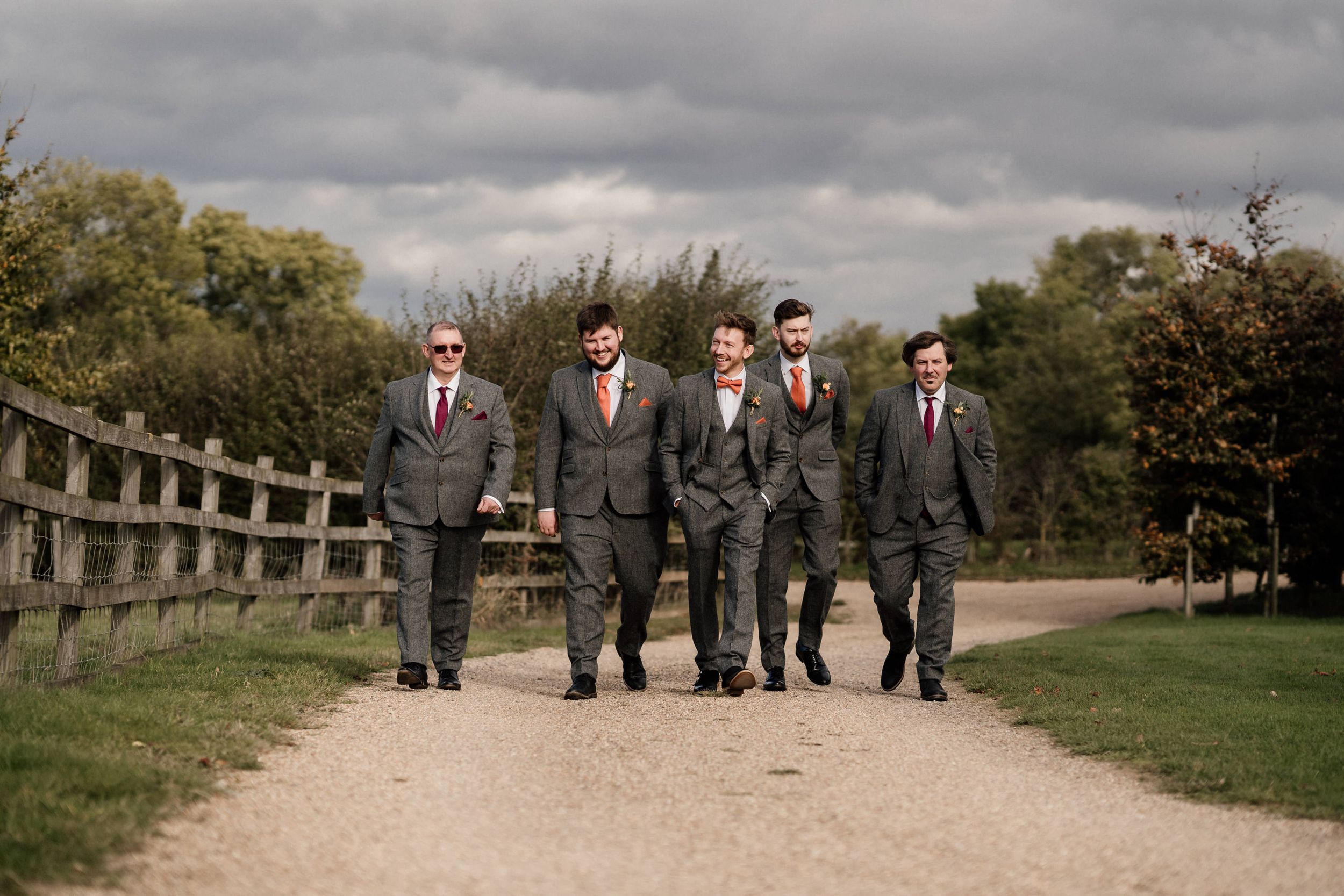 Groomsmen in gray suits walking together on a countryside path at Dodford Manor.