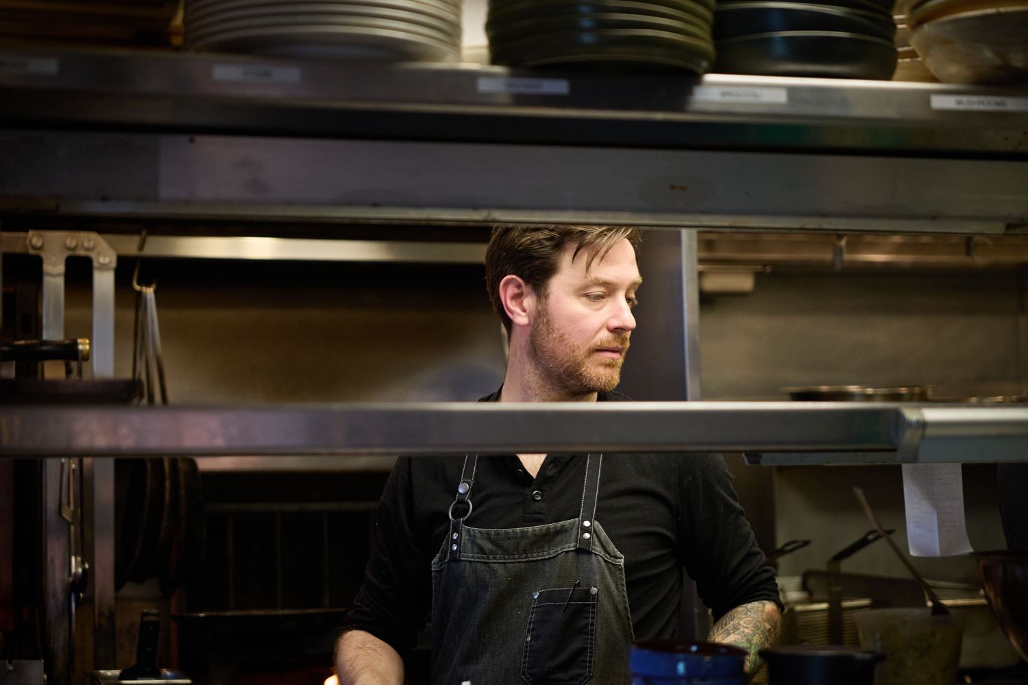 Chef in dark clothing working in a commercial kitchen with stacked plates visible.