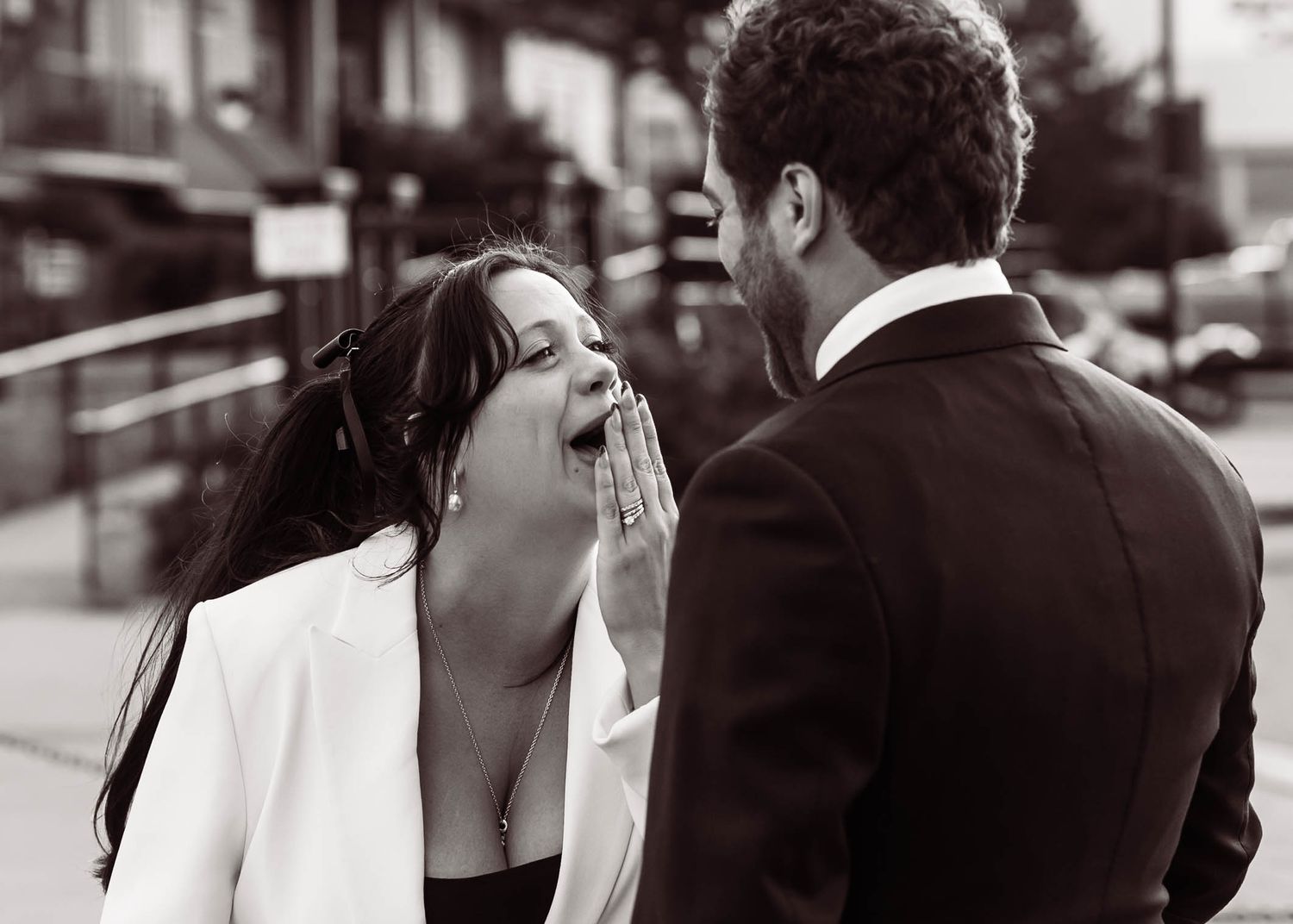 A candid black and white photo captures a joyful moment between a couple sharing laughter on a city street.