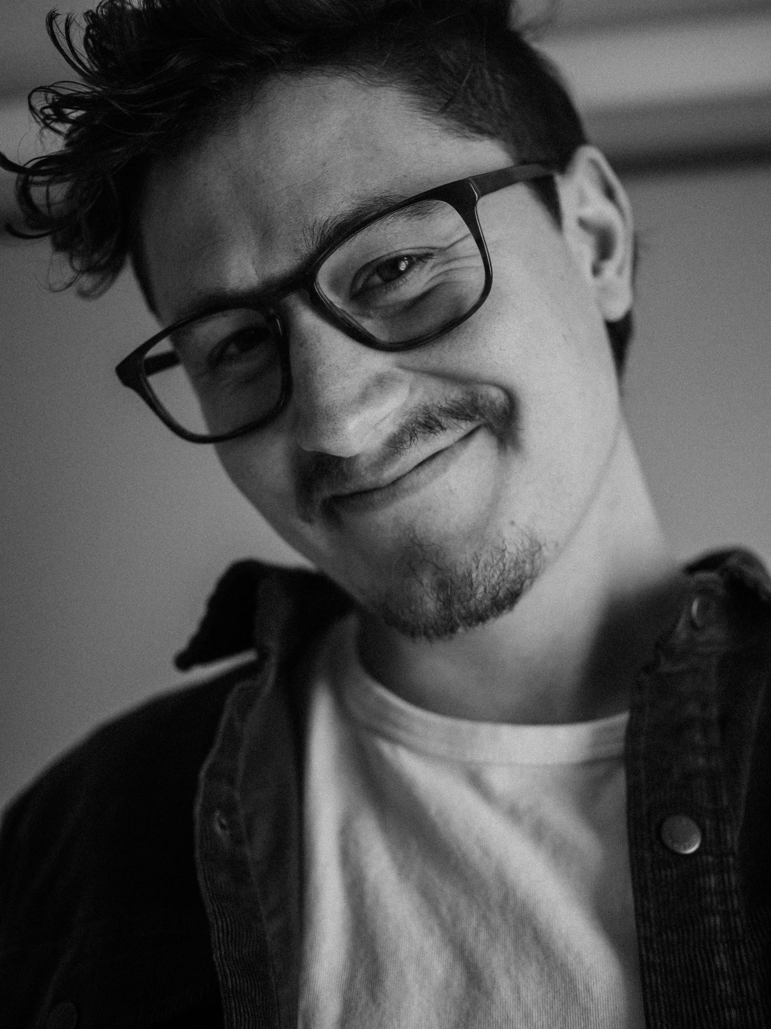 Black and white portrait photo of someone in glasses, cardigan and white t-shirt smiling warmly at the camera.