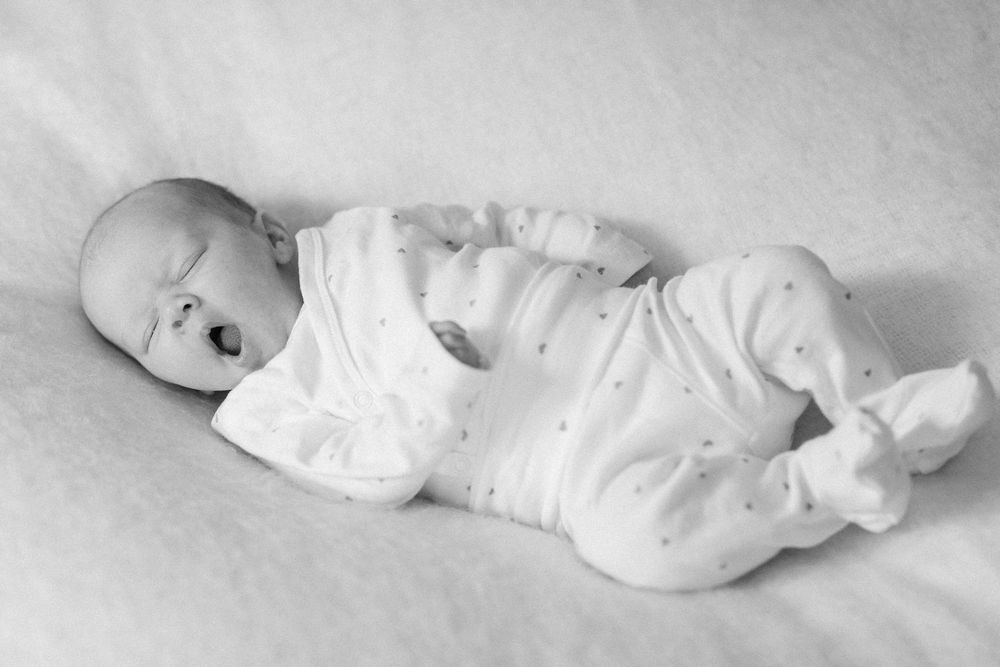 Black and white photo of an infant wearing a white onesie lying on a light colored surface.