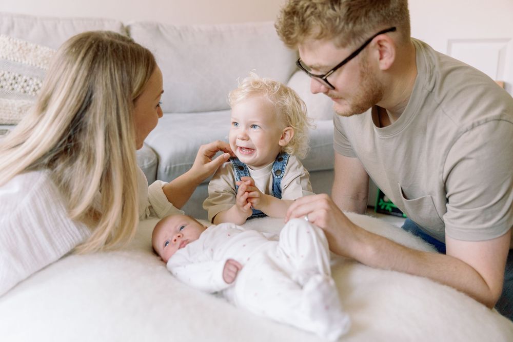 Parents share a tender moment with their happy toddler while relaxing together on a white couch.