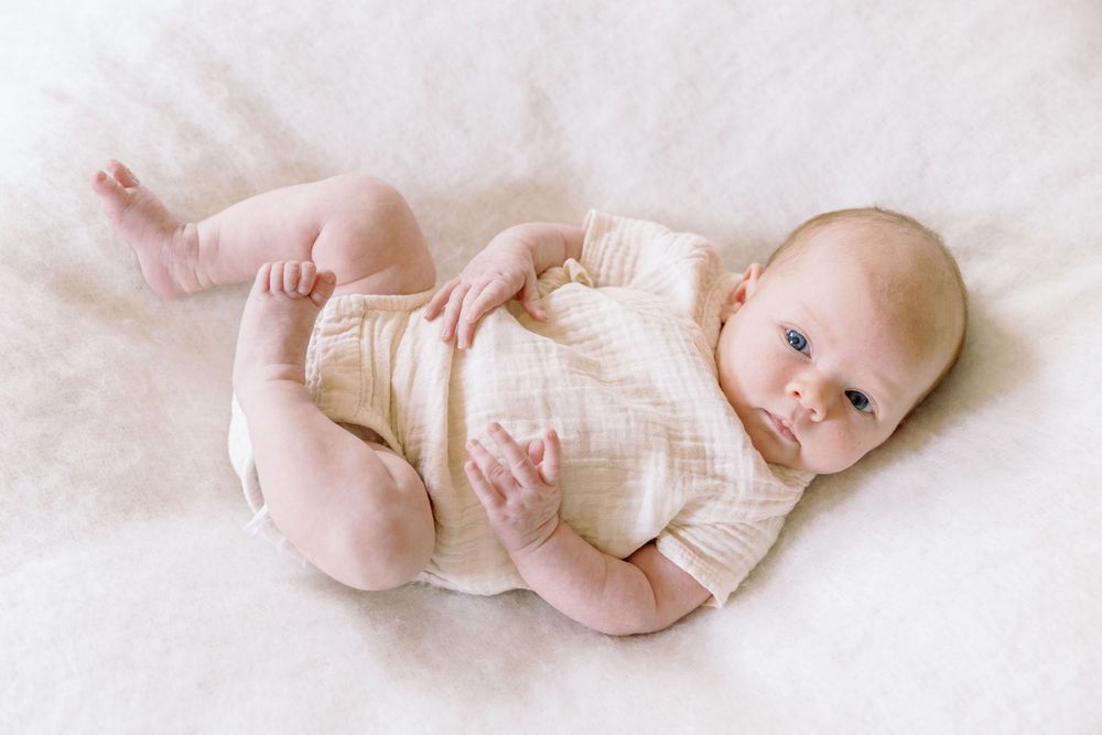 Baby wearing cream-colored linen romper lying on soft white blanket.