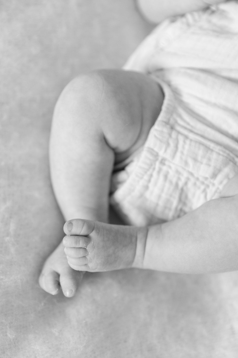A black and white close-up of a baby's tiny bare feet and legs against white fabric backdrop.