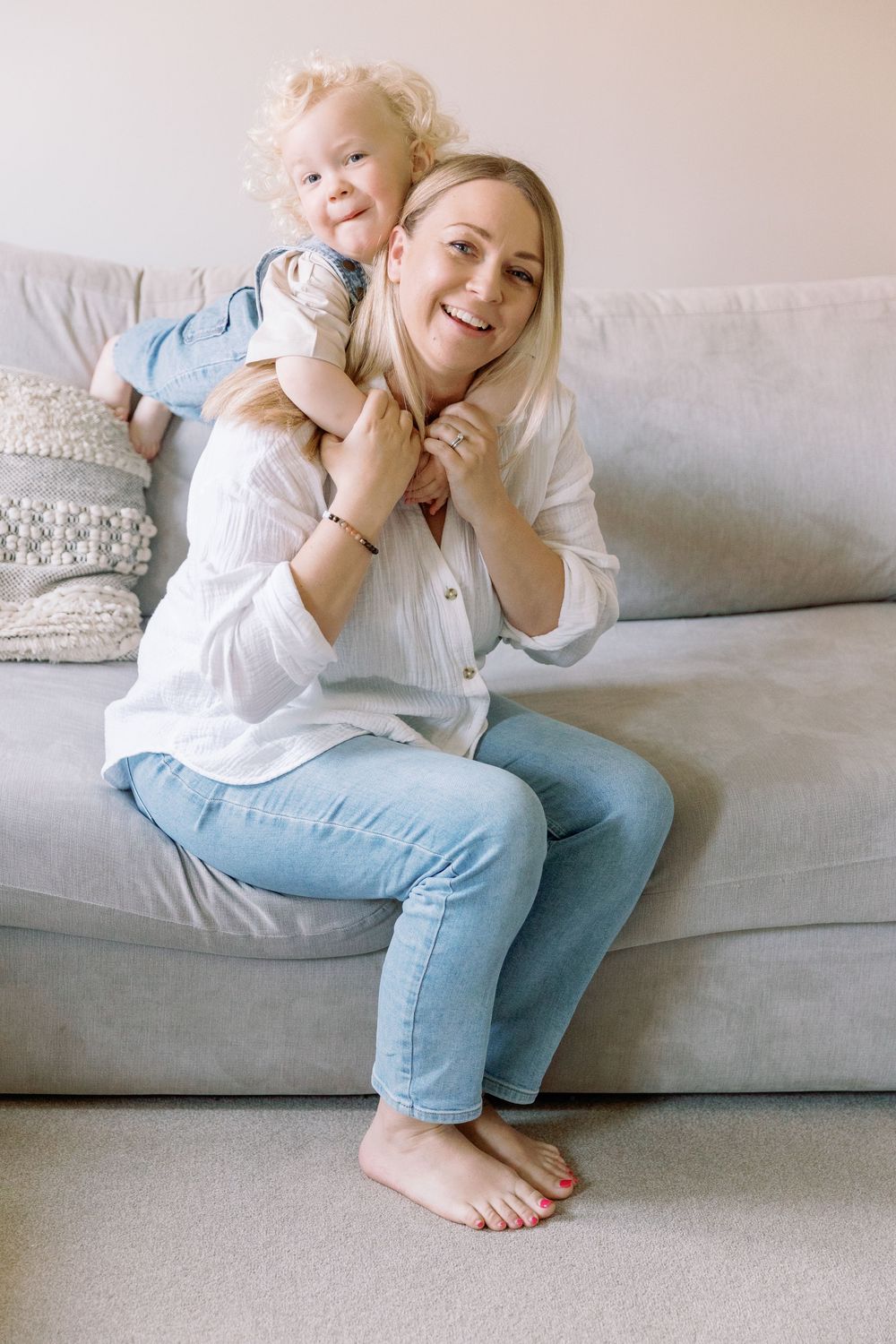 A loving embrace shared on a comfortable gray couch, with a white button-down shirt and light denim jeans creating a casual mood.