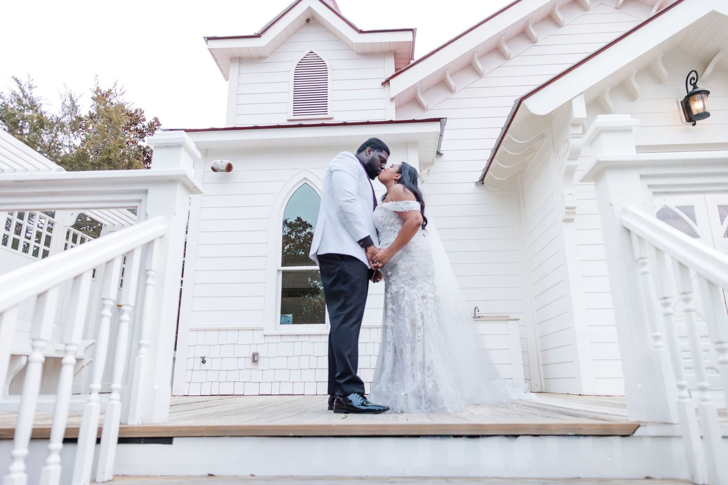 Couple in wedding attire sharing a romantic dip kiss under a white Gothic-style church archway.