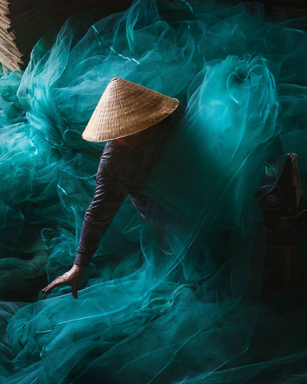 Figure in traditional conical hat surrounded by ethereal turquoise smoke creates mysterious atmospheric scene.