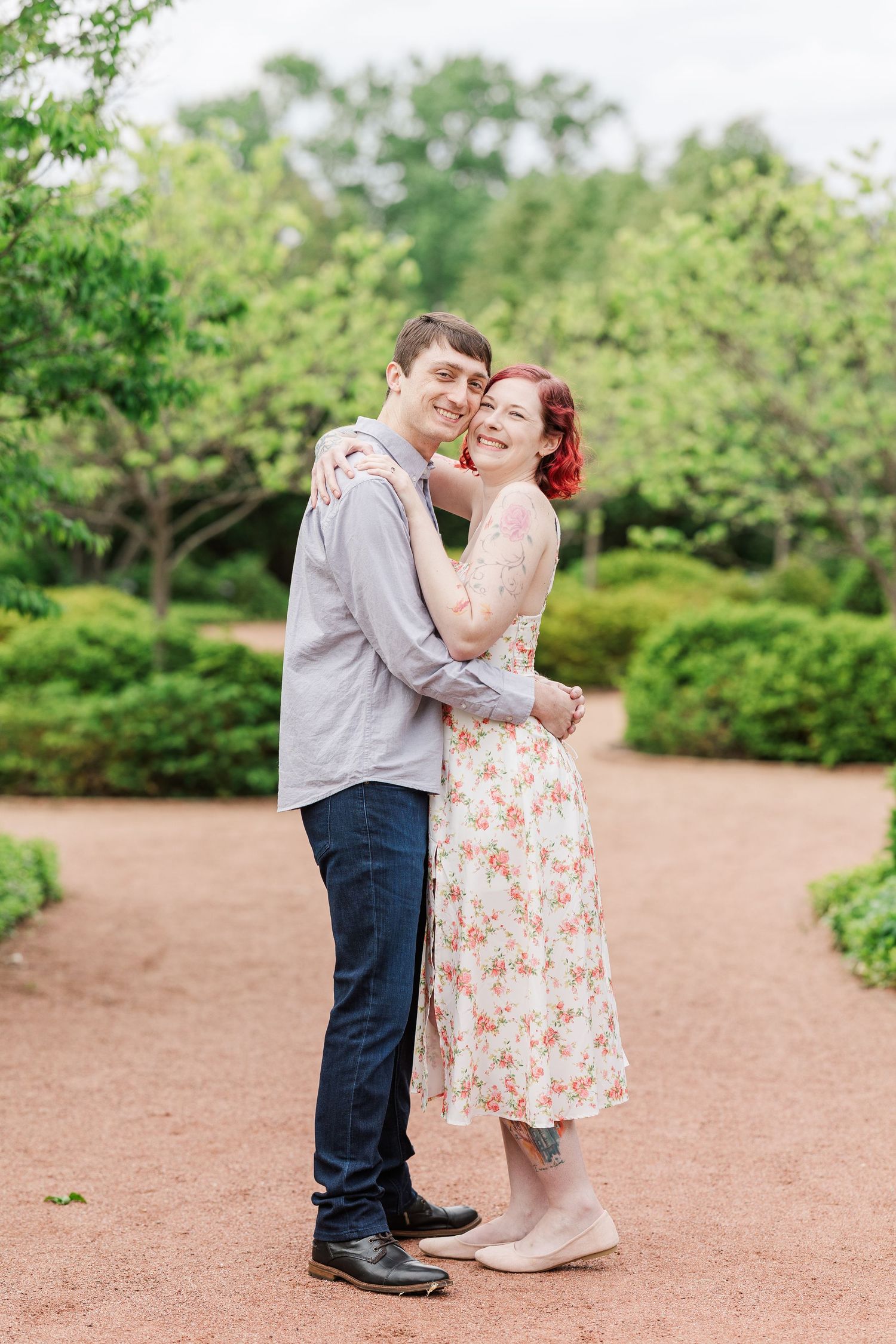 A romantic couple embraces on a garden path surrounded by lush green landscaping and trees at Cantigny Park