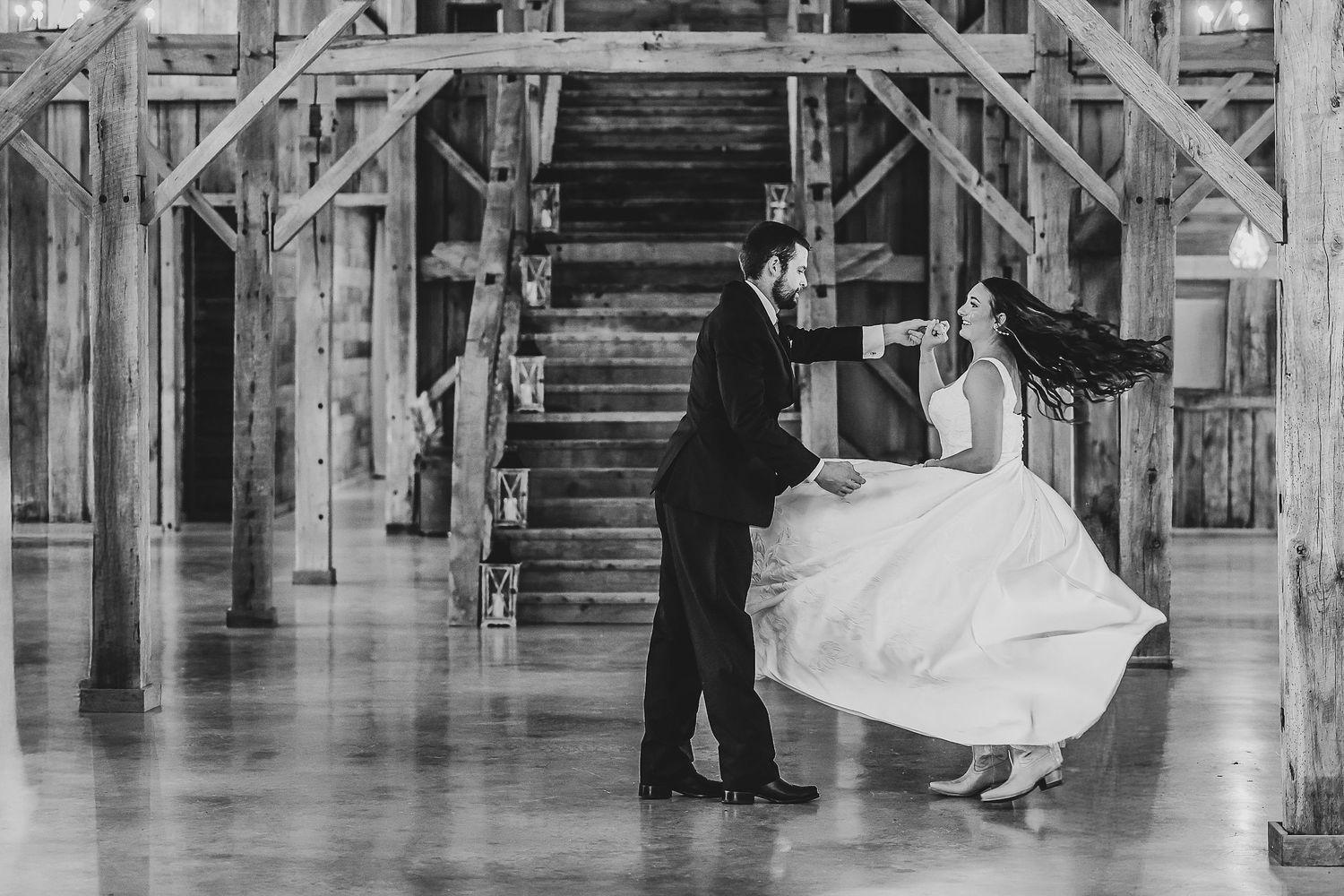 a black and white photo of the bride and groom having their first dance in front of the staircase of the madelyn wedding venue