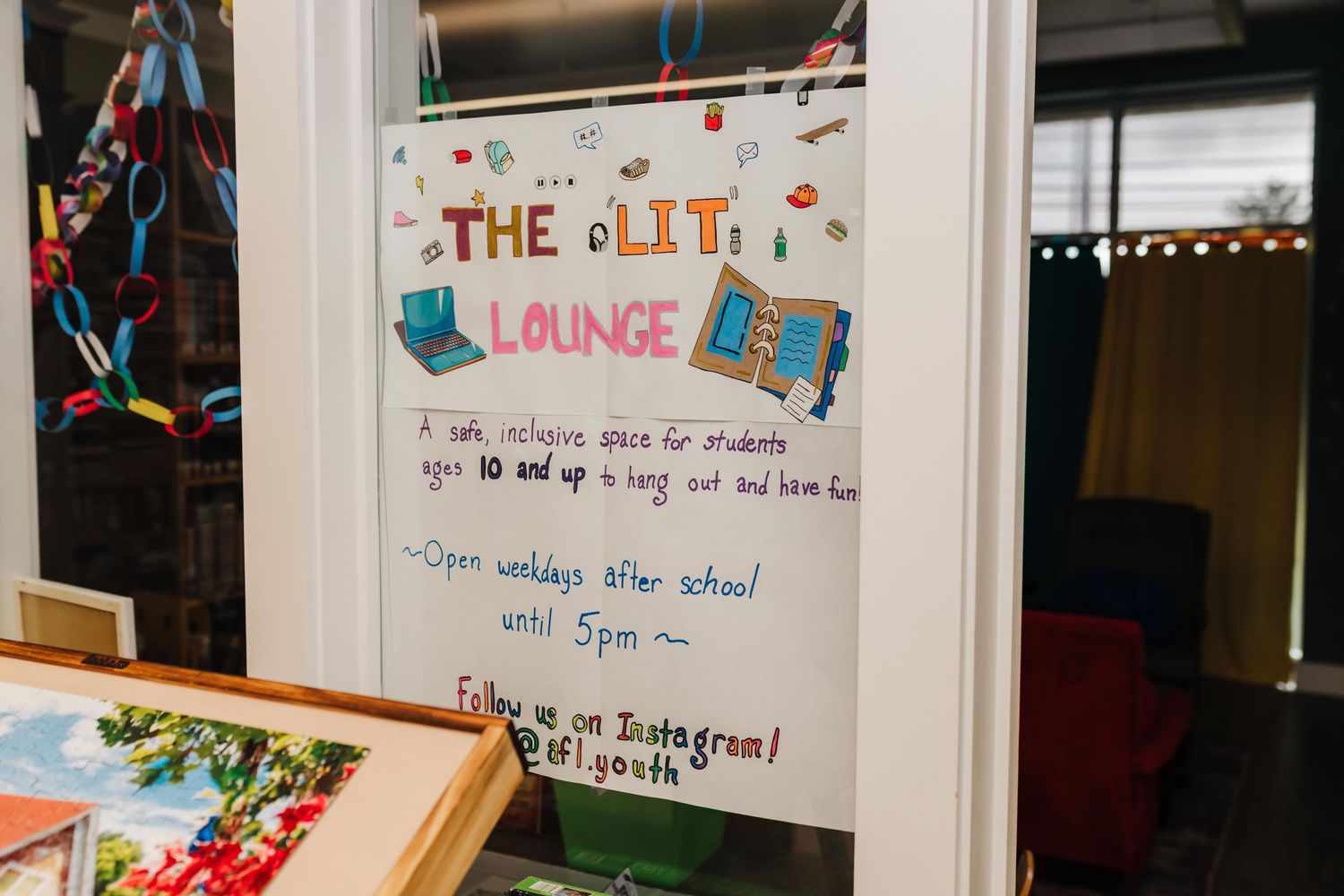 A handmade sign for "The Lit Lounge: A safe, inclusive space for students ages 10 and up to hang out and have fun." on the door of a room.