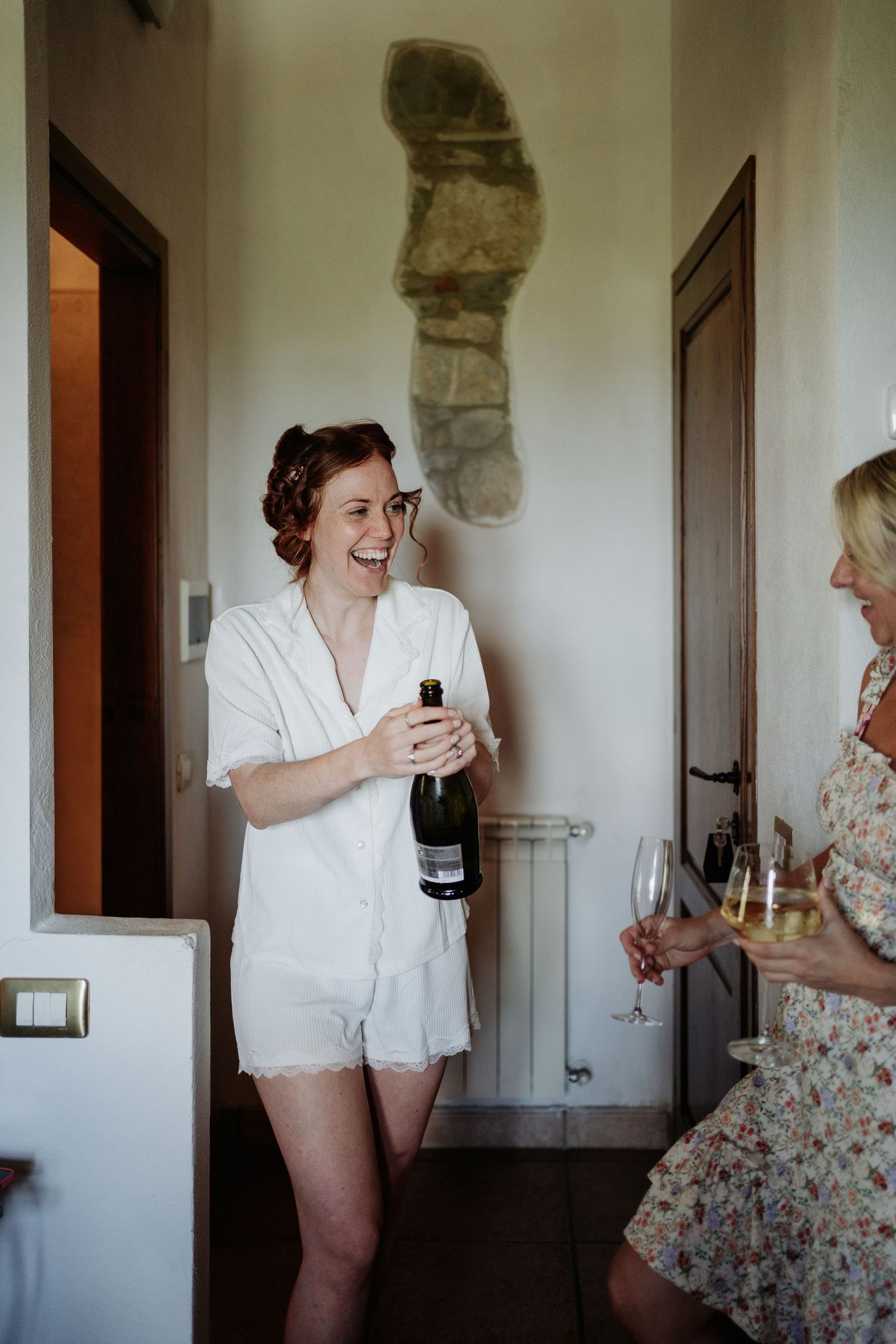 Bride popping Champagne during morning of Italian wedding at Villa Le Bolli