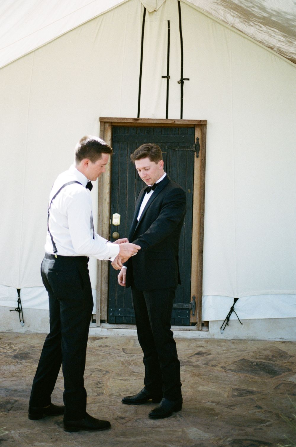 Two men in formal attire checking time and adjusting watches before event.