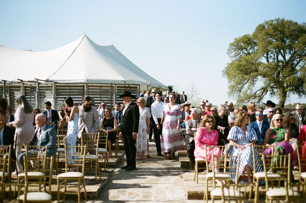 Wedding guests gather under a large white tent for an outdoor celebration.