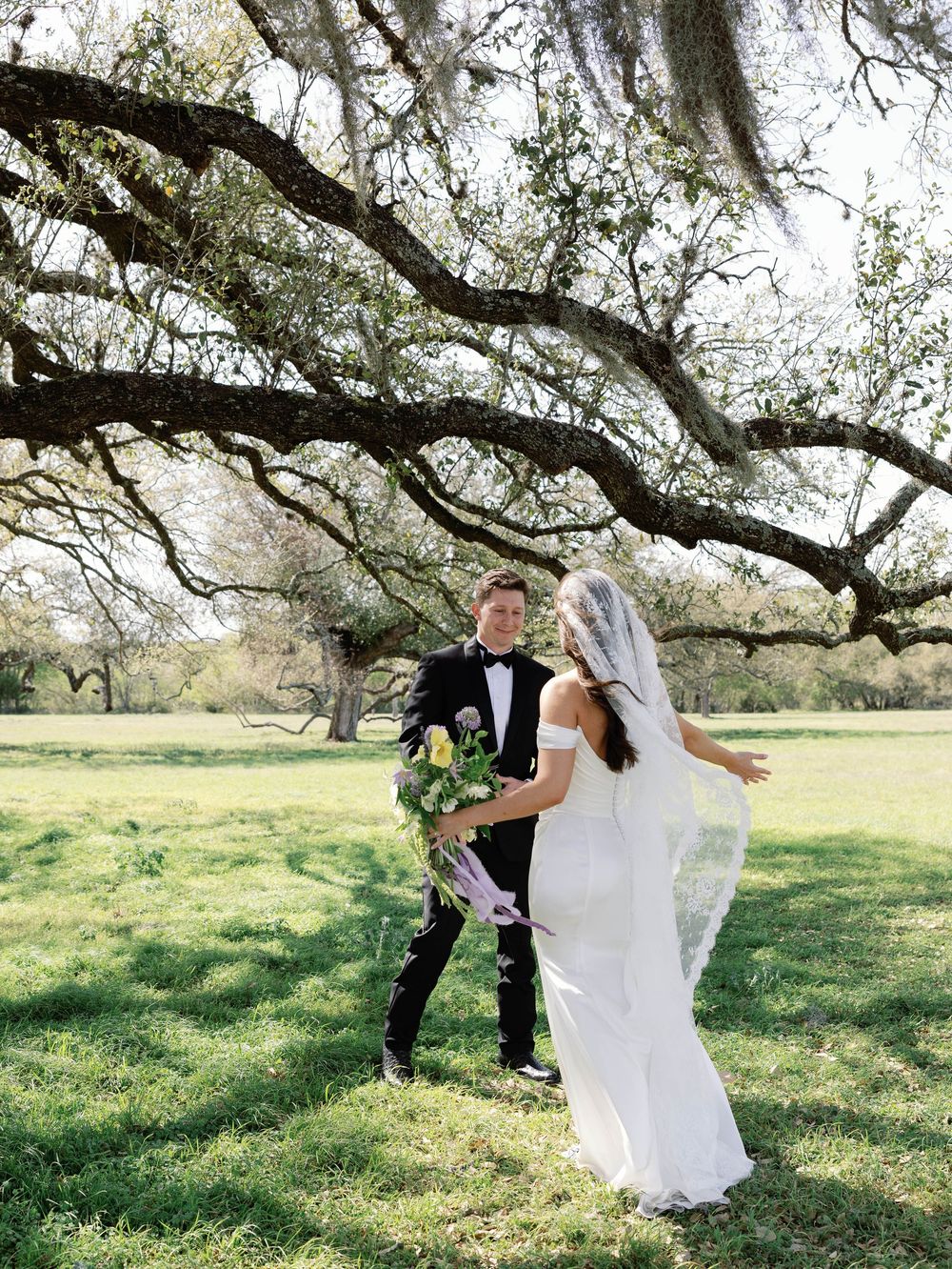 A couple shares a romantic moment under Spanish moss-draped oak trees in an outdoor wedding setting.