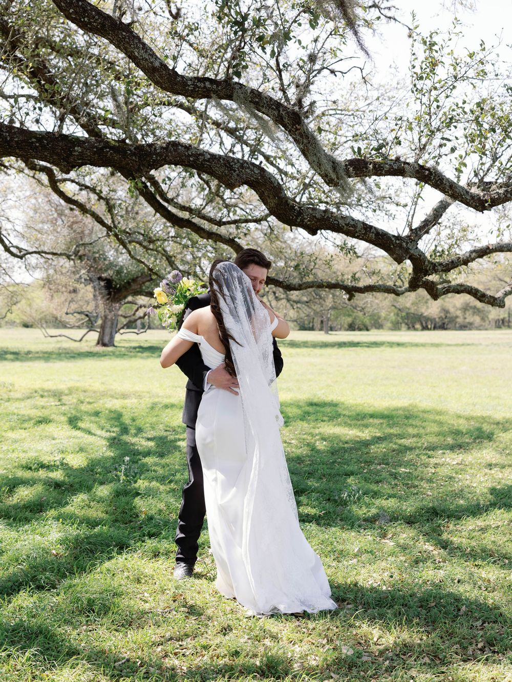 Bride and groom share intimate moment under sprawling oak tree in outdoor setting.