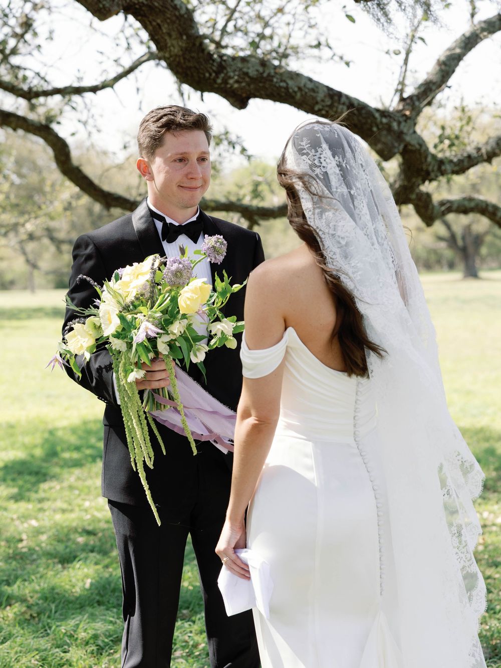 Groom holding beautiful spring bouquet during first look with bride in outdoor setting.