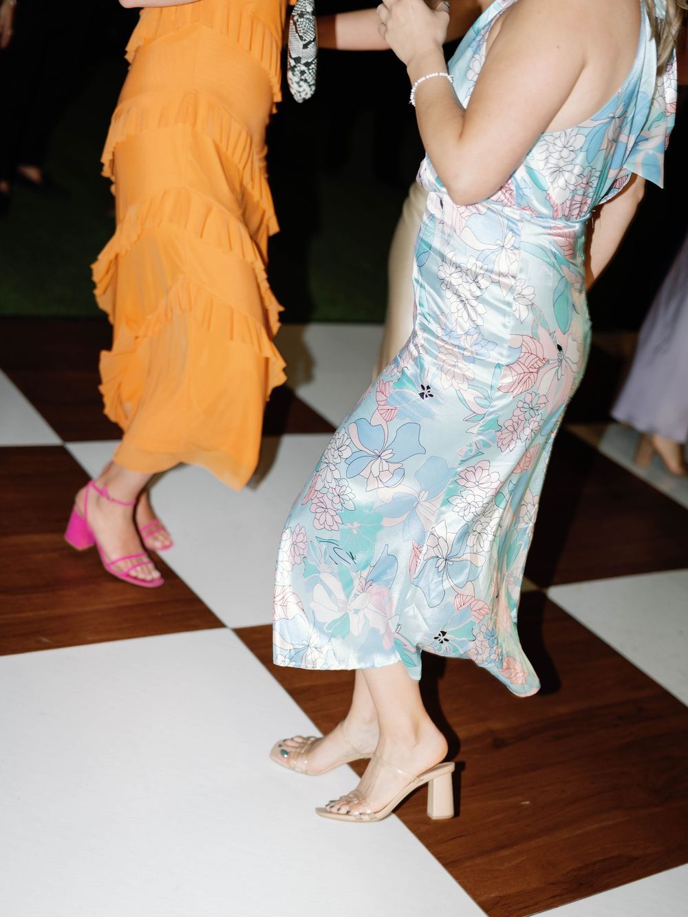 Wedding guests in colorful dresses dancing on checkered dance floor.