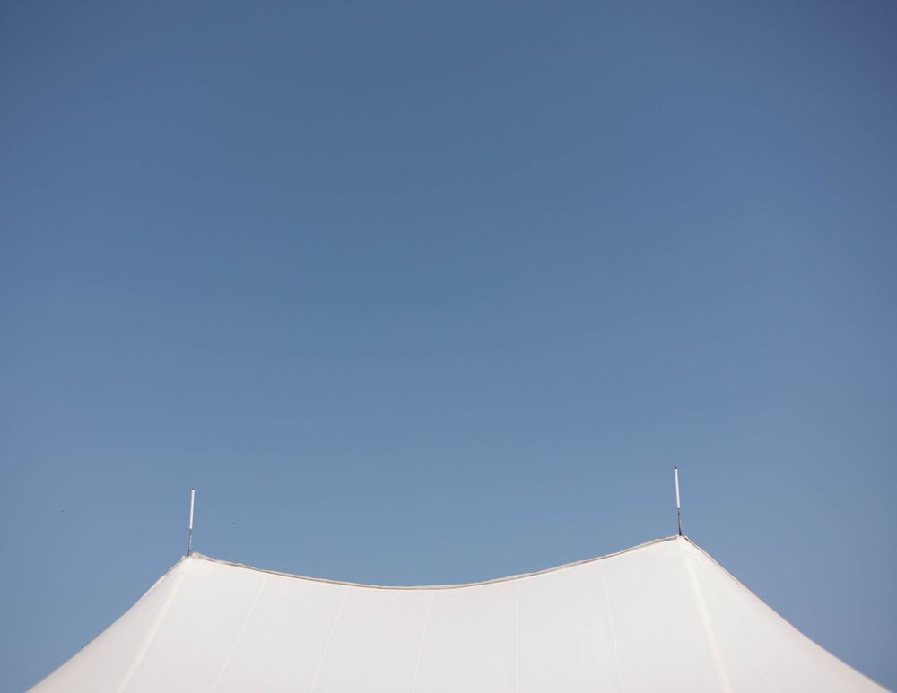 Top peaks of a white tent against bright blue sky with minimal design.