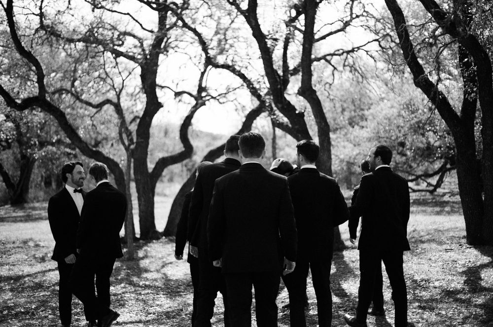 Black and white photo of a group gathered under twisted tree branches outdoors.
