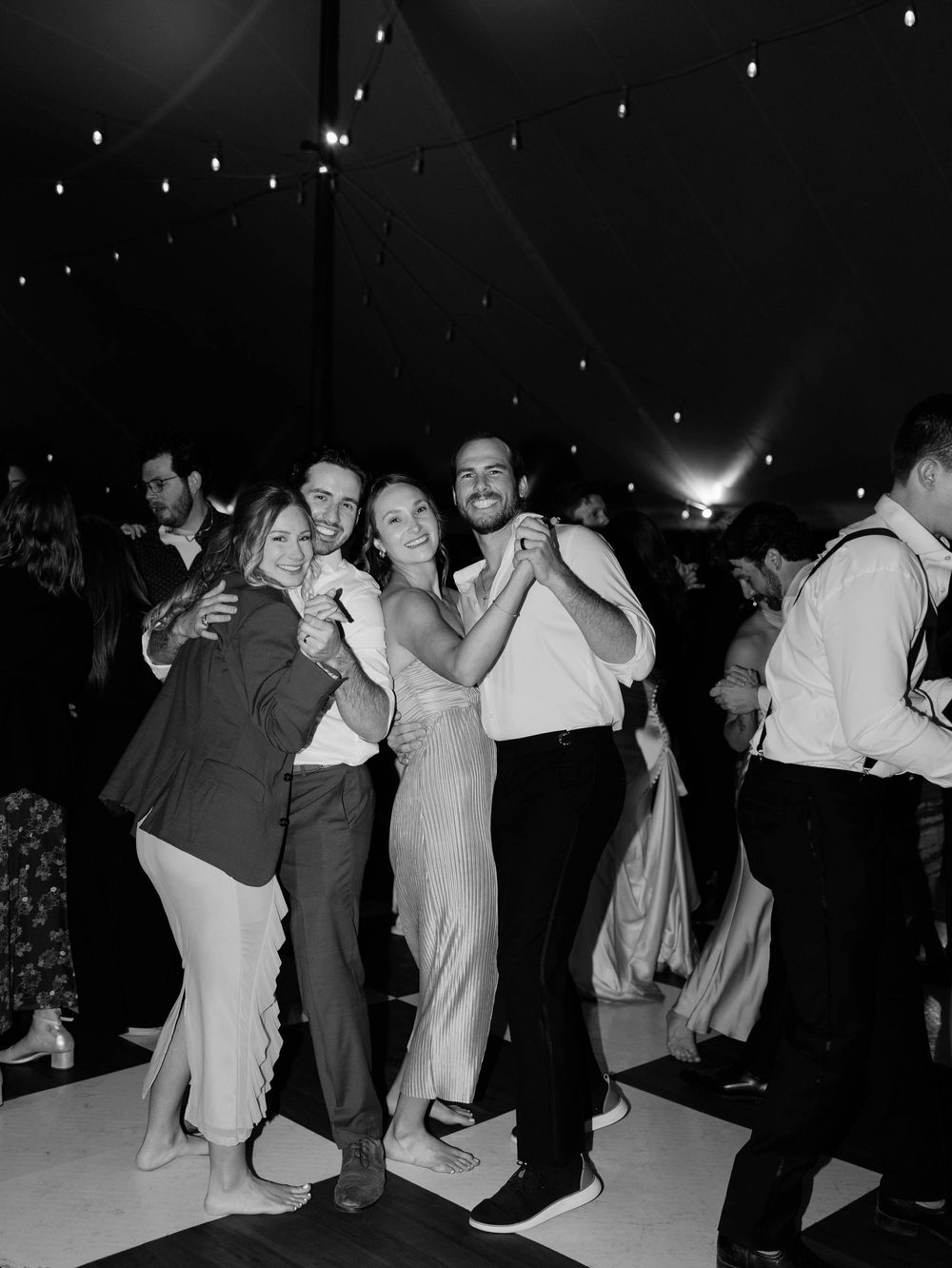 Group of wedding guests dancing and celebrating under string lights at night.