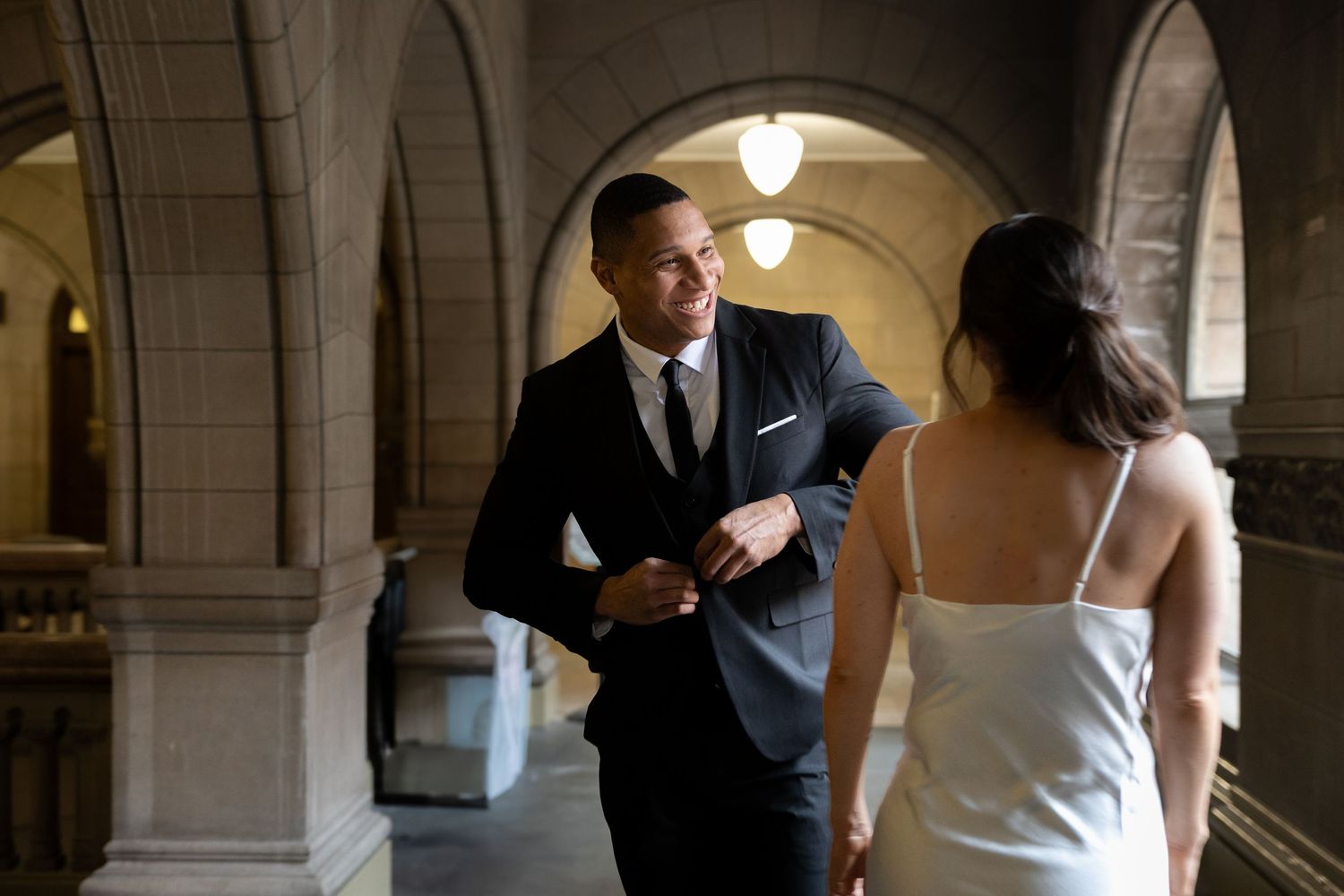 A happy couple shares a moment in an elegant arched hallway as they get ready for their wedding ceremony.