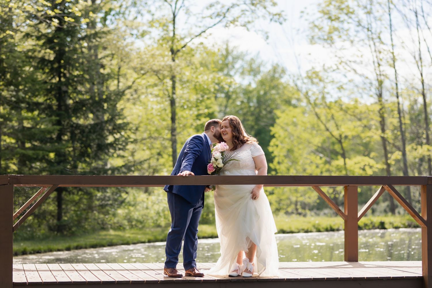 A tender embrace shared on a wooden deck surrounded by lush green forest scenery on a bright sunny day.