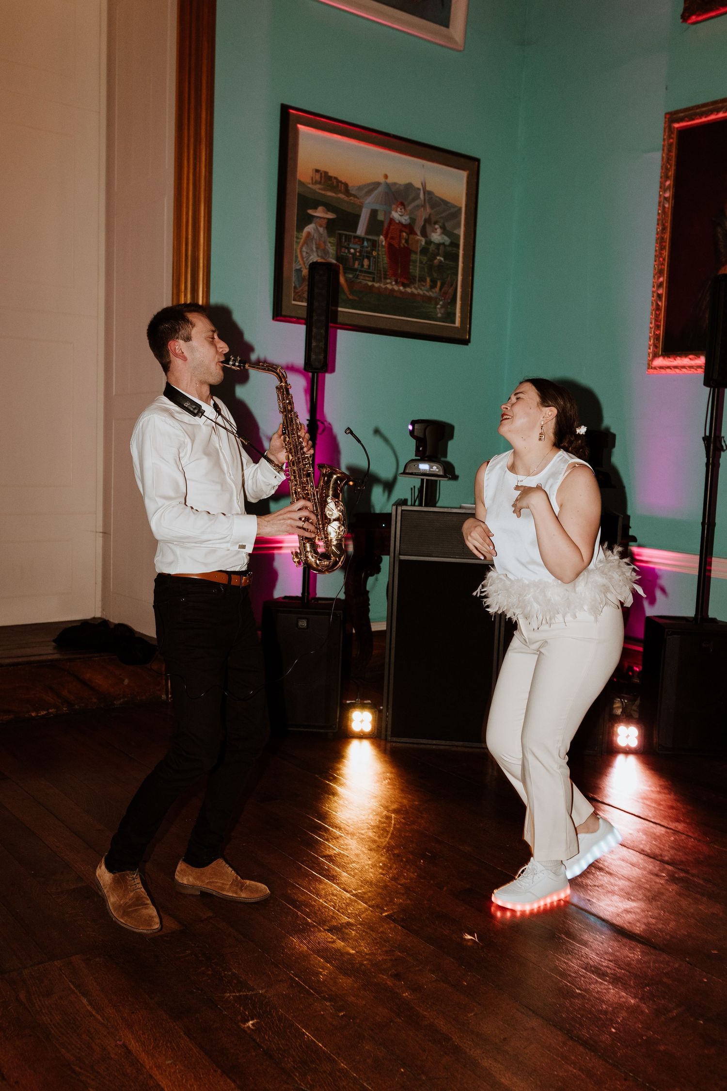 Musicians perform at a wedding reception with saxophone player and singer on a hardwood floor in a room with teal walls.
