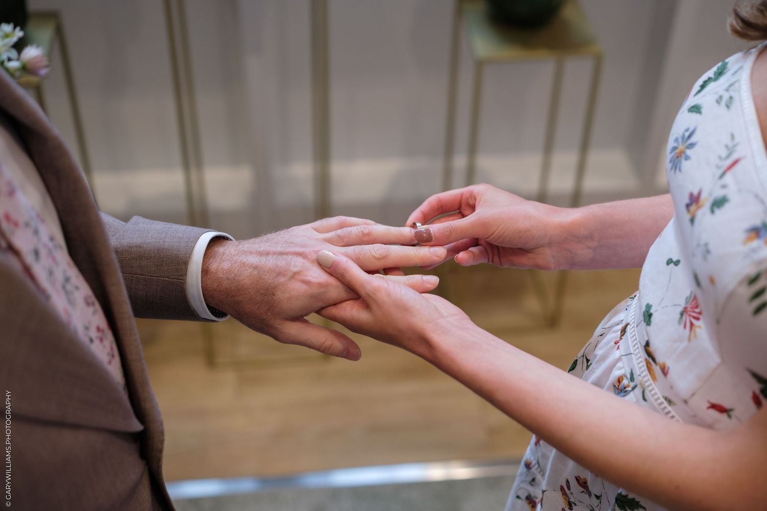 Close up of hands as someone puts a ring on another person's finger during a wedding ceremony.