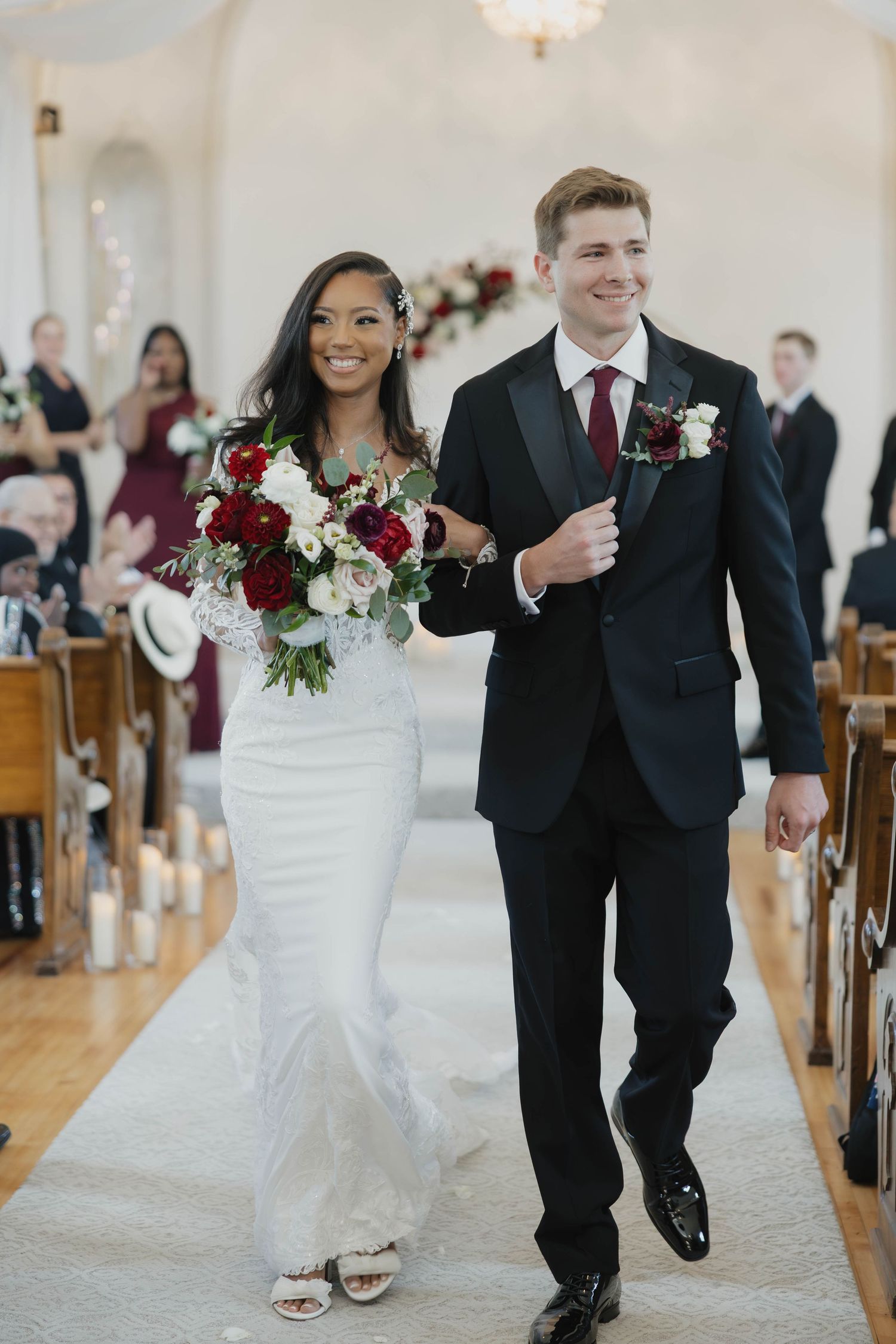 A bride and groom walk down the church aisle after their wedding ceremony, with red and white floral bouquet details.