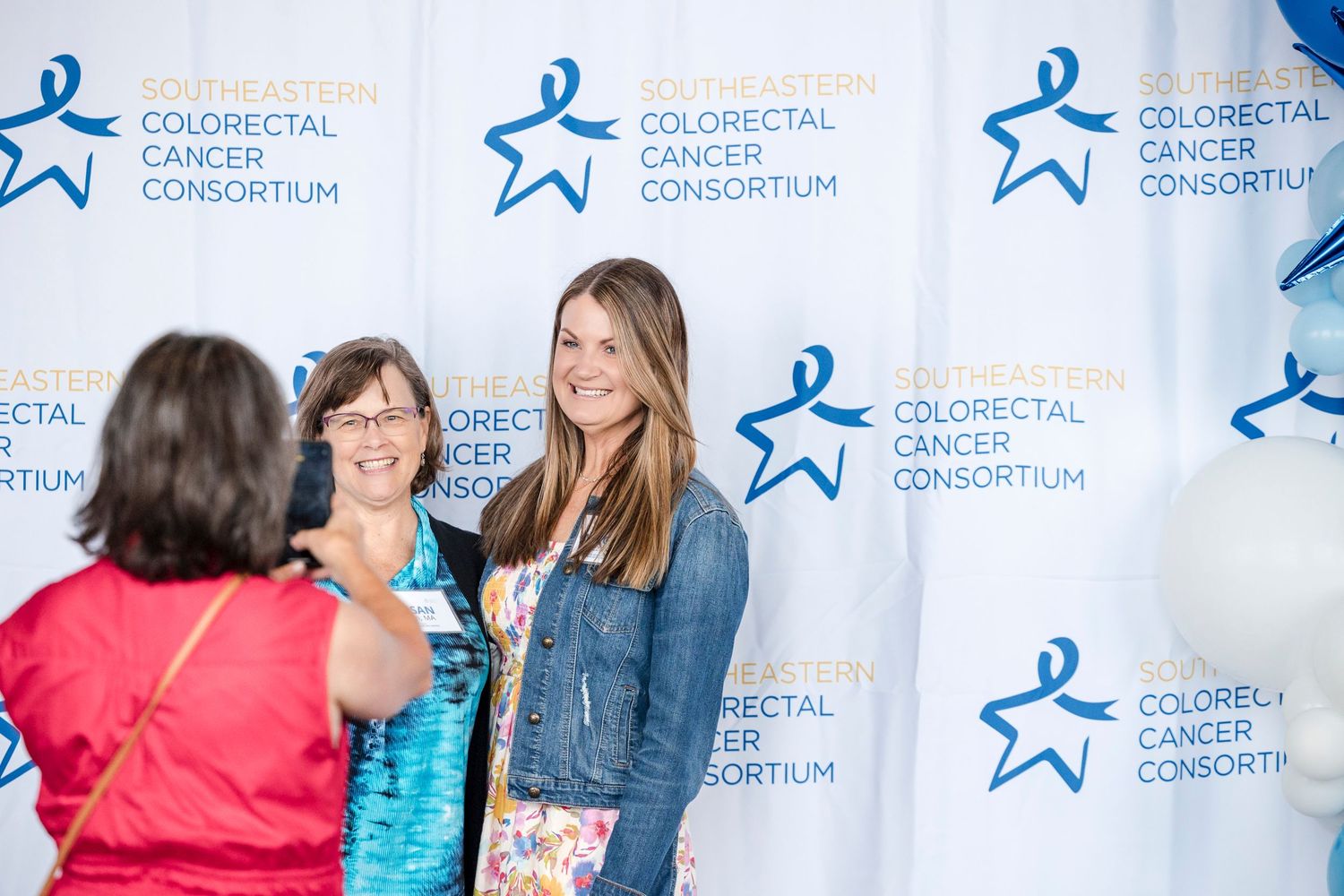 People interacting at a Colorectal Cancer Consortium event with promotional backdrop featuring blue star logos.