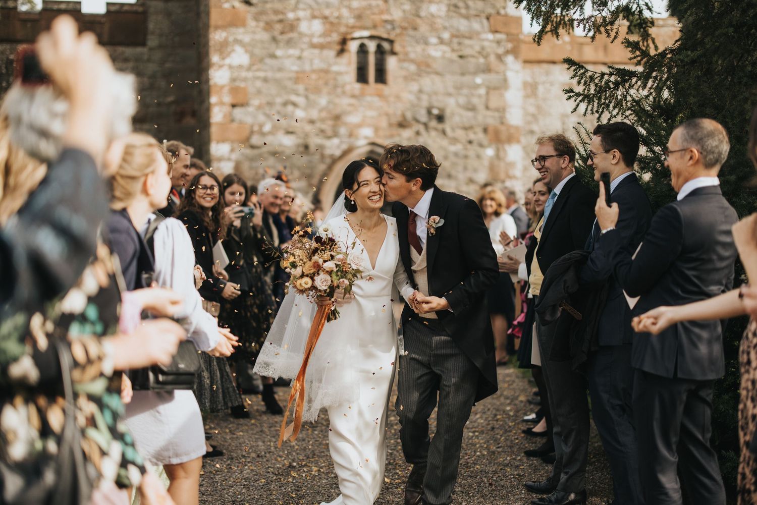 Wedding guests shower newlyweds with confetti while exiting the church of Askham Hall on their special day.