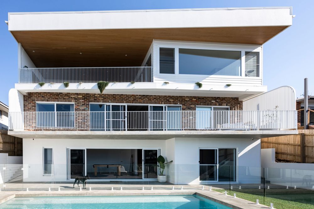 Modern three-story luxury home with clean lines, glass balconies, and a swimming pool in the backyard.