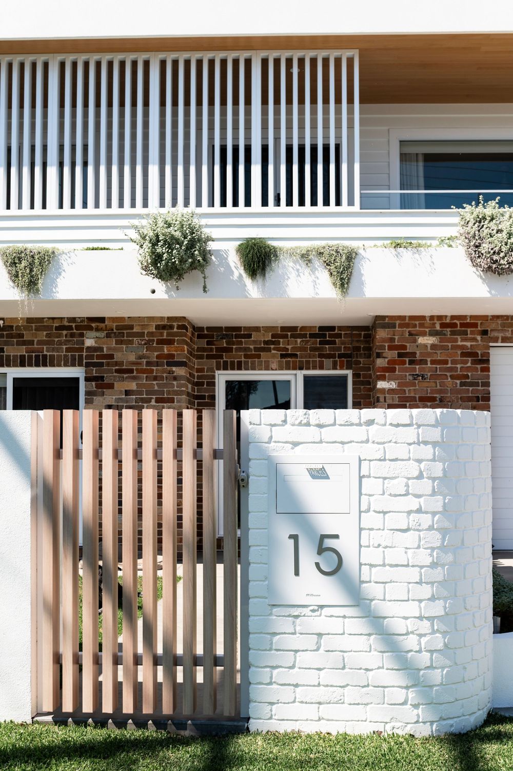 A series of white brick walls with wooden slat gates and house numbers displayed against painted brick surfaces.