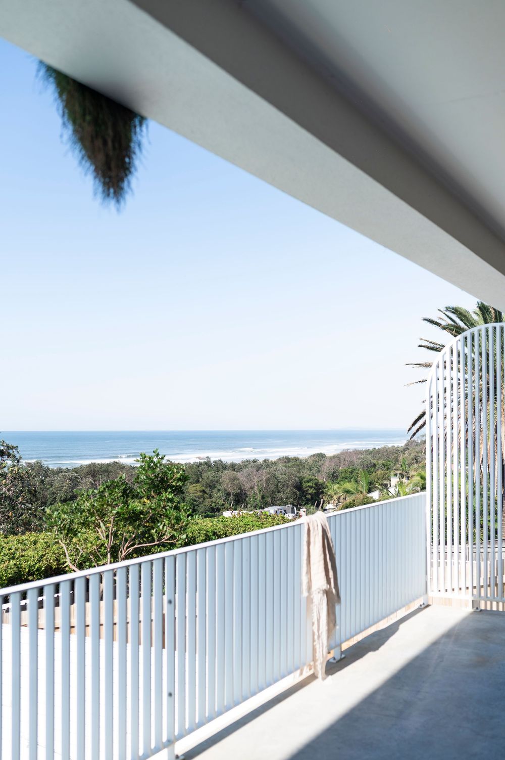 White coastal balcony with vertical railings offering panoramic ocean and landscape views.