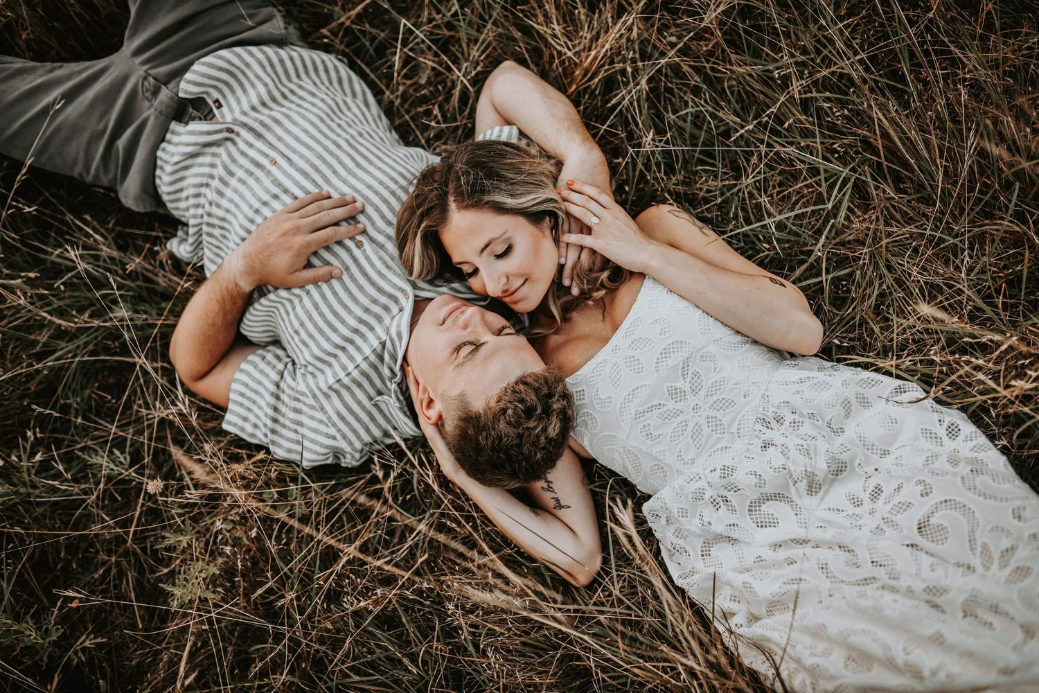 Sunset light beaming behind a couple sharing a forehead kiss in golden grass as they lay on the grass