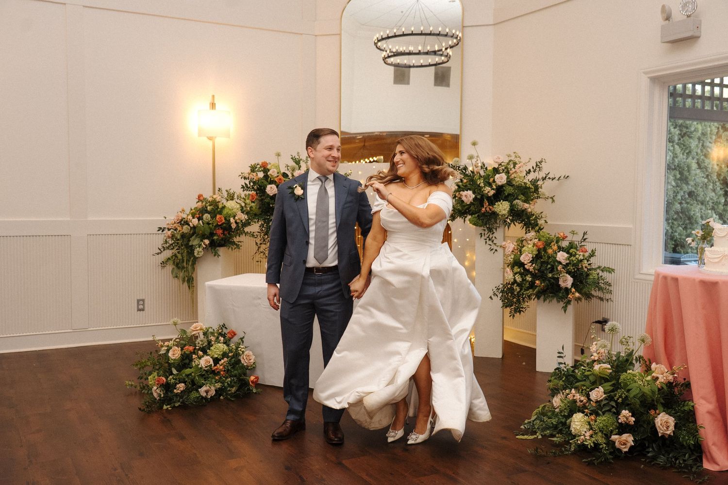 Couple dancing at a wedding reception with floral arrangements and white walls in an elegant venue.