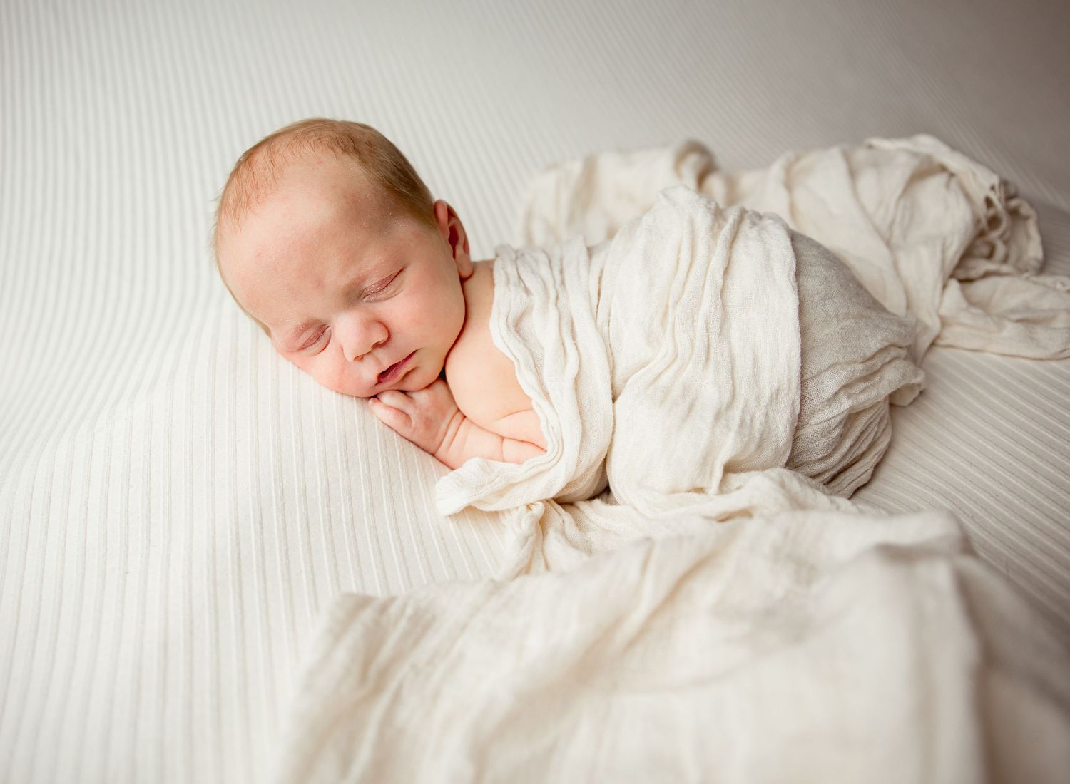 A sleeping newborn baby lies peacefully in soft white bedding during a professional photography session.