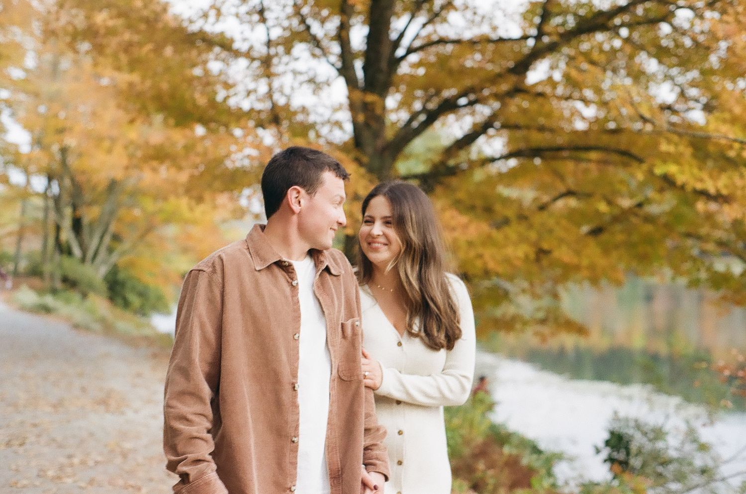 Romantic fall engagement photo with couple against autumn foliage near river.