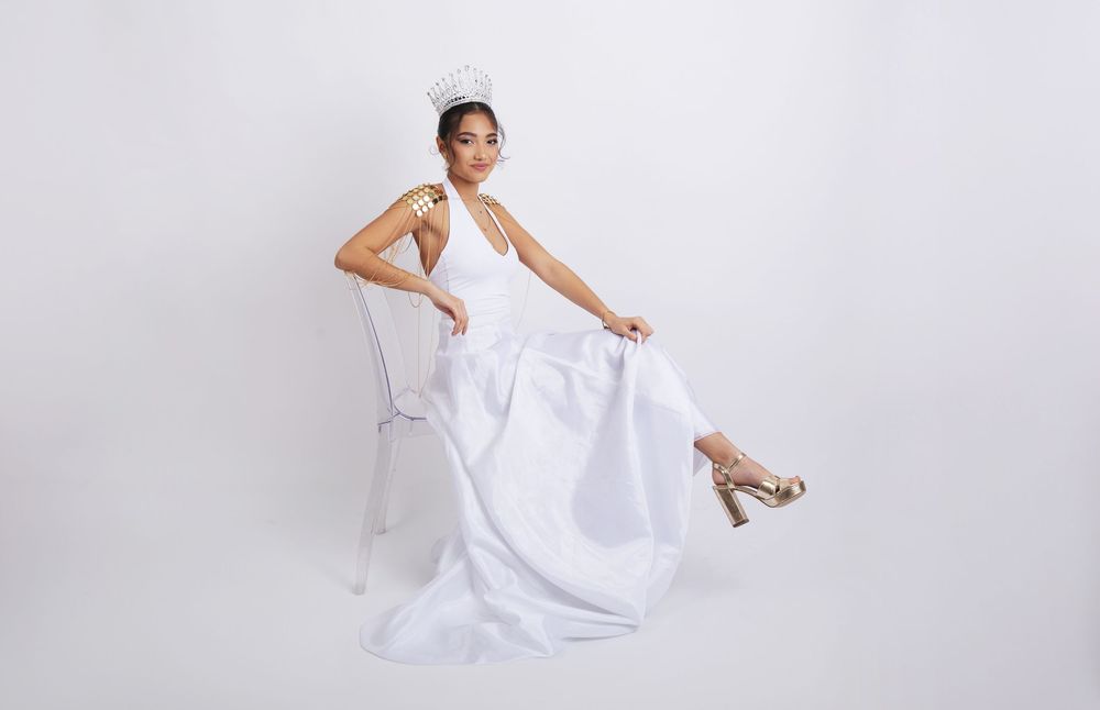 A graceful figure in a flowing white gown poses elegantly on a light backdrop while wearing strappy high heels.