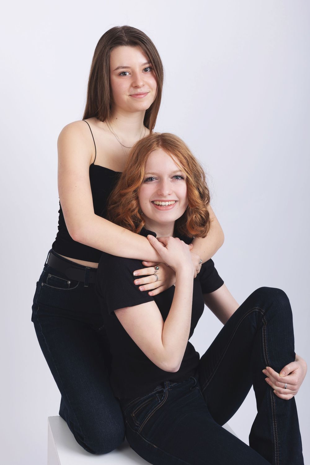 Two friends wearing black outfits pose together against a white background in an intimate portrait session.