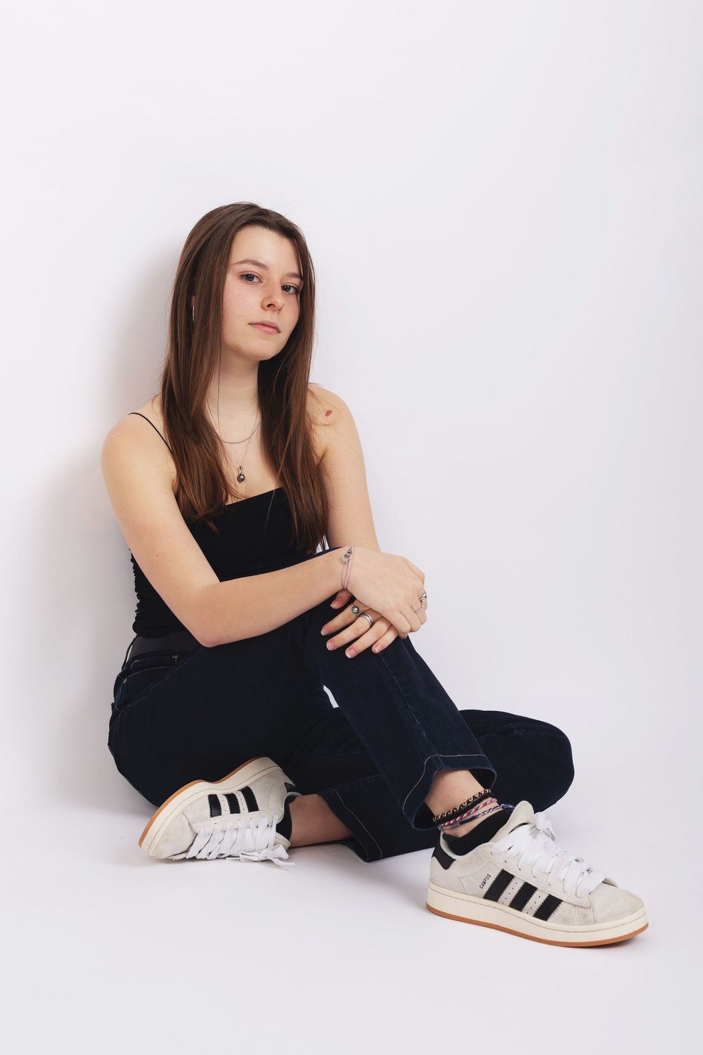 A casual portrait against a white backdrop featuring Adidas sneakers and dark casual wear.