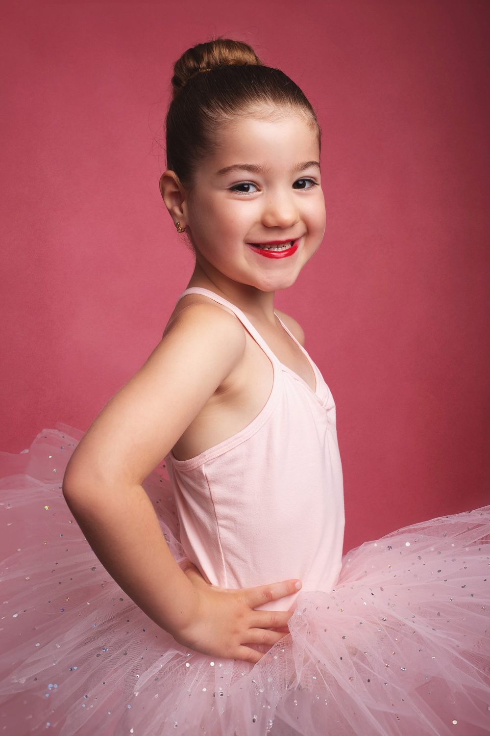 Young ballet dancer in pink tutu poses against rose-colored background during dance portrait session.