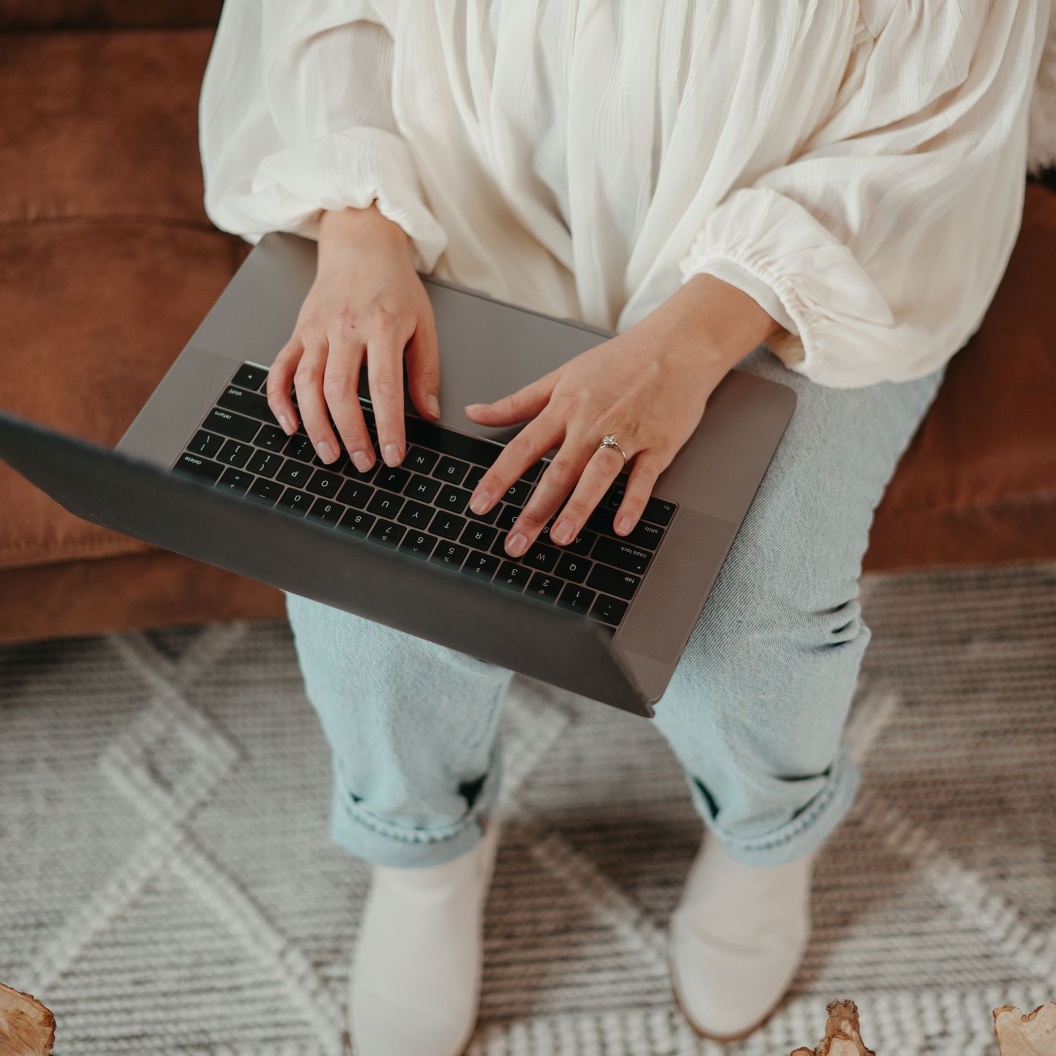 Top view of hands typing on laptop keyboard while wearing white sweater and jeans.
