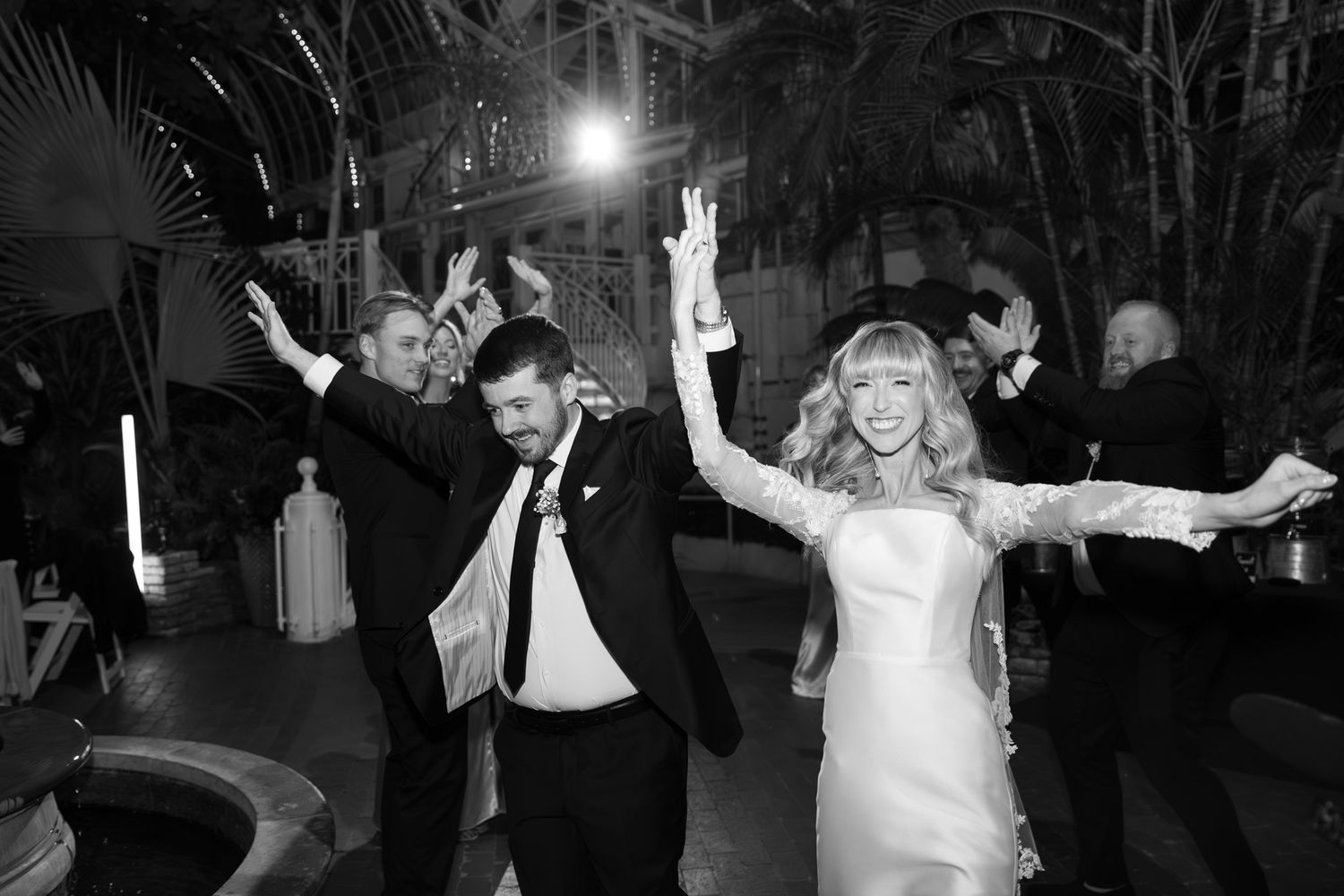 Wedding reception guests dancing and celebrating in a dimly lit venue.