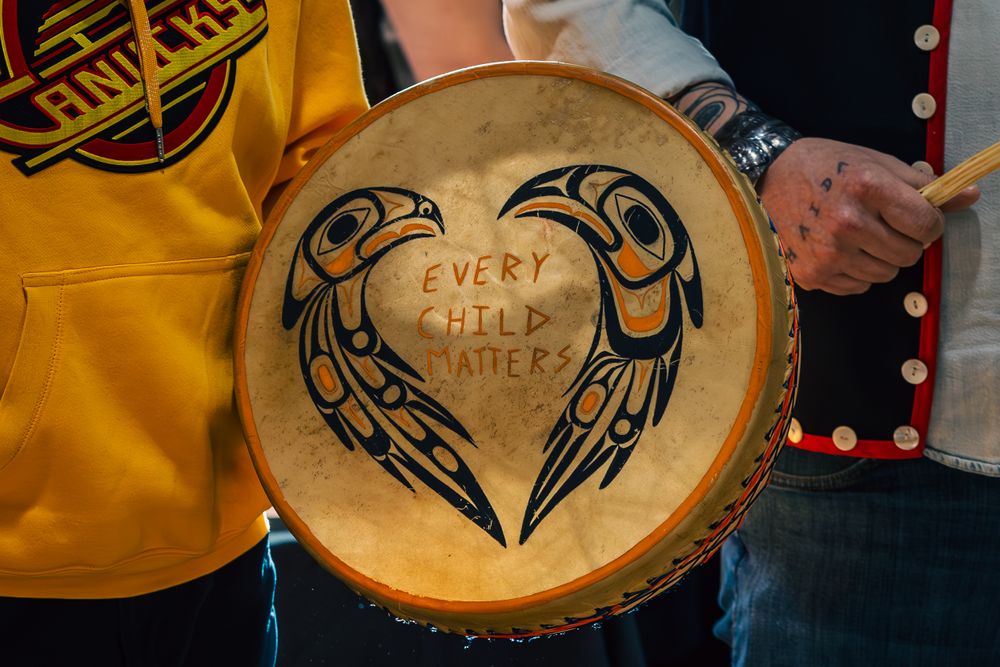 Haida hand drum decorated with black tribal raven design and text against natural wood background.