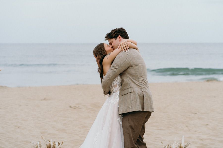 A couple embracing on a beach during their wedding day.